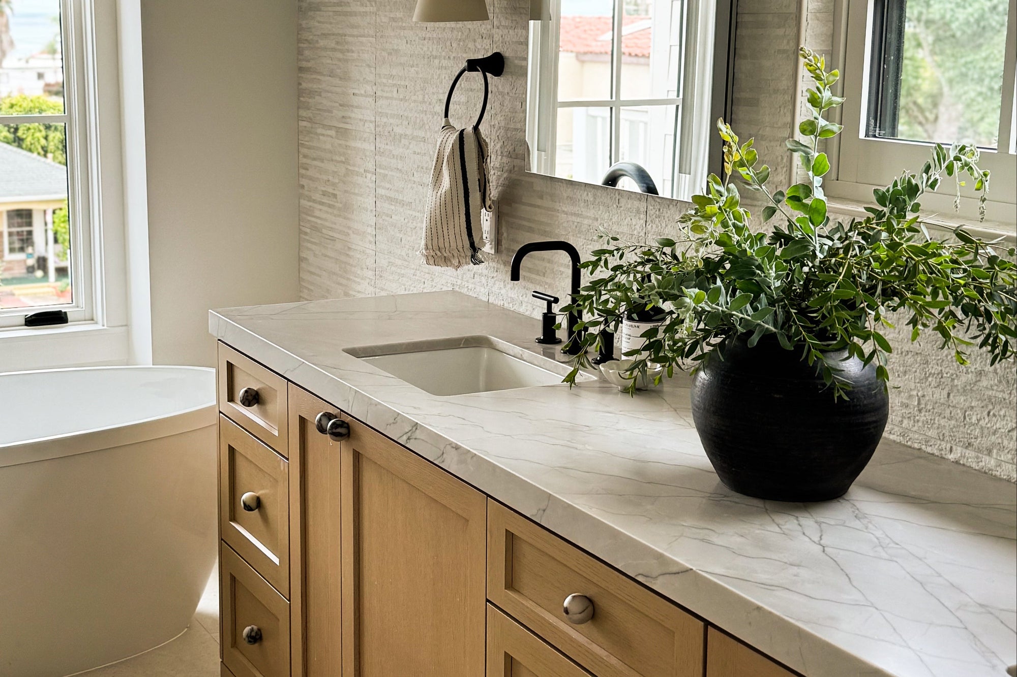 Modern bathroom with freestanding bathtub, wooden vanity, and large windows. Vance Design Co Interior Designer