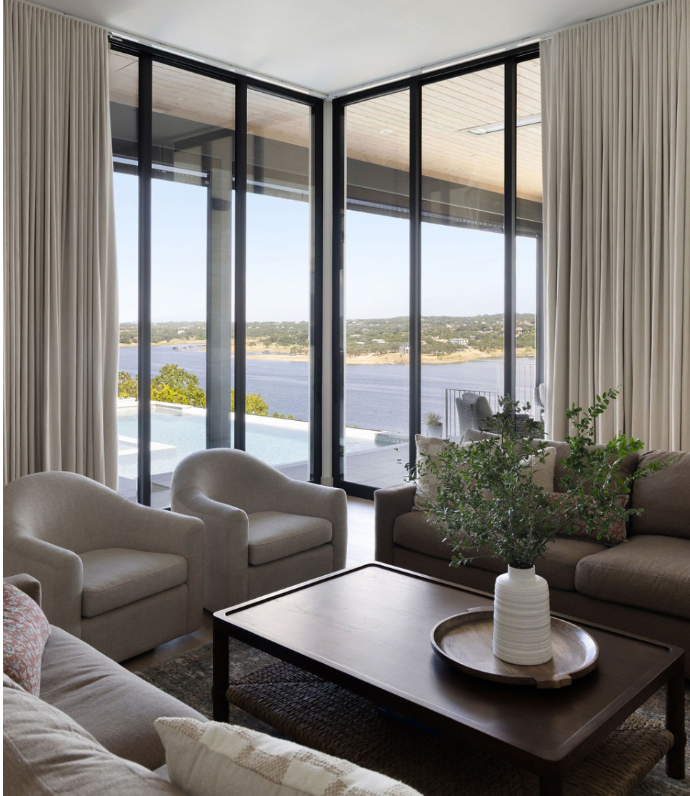 Lake-view living room with neutral seating, full-height curtains, and a wood coffee table.